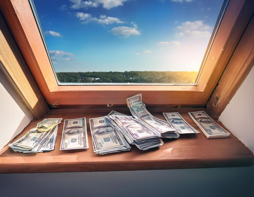 Plik banknotów dolarowych leżący na parapecie w trakcie wymiany okna dachowego.